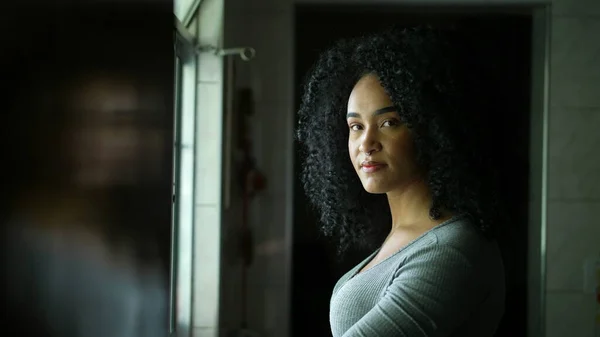 A contemplative young woman standing by window looking outside