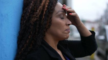 Stresli bir Afrikalı kadın sokakta duvara yaslanıyor.