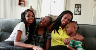 Black African mother and teen daughters and little boy son together at home sofa