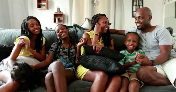 Casual African family sitting at home living-room. Black parents and children together in sofa