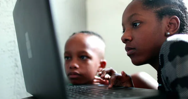 Black teen girl staring at computer screen, little brother watching sister browse the internet