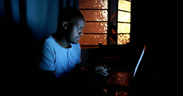 Black man in front of laptop computer at night, person working late