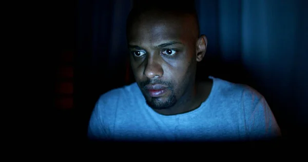 Black man face staring at laptop screen at night