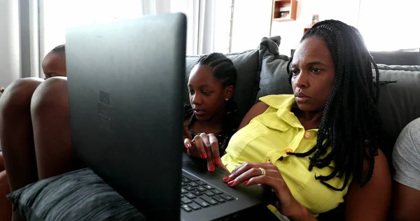 Black African mother watching laptop screen at home sofa with kids