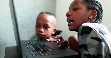 Genç Afrikalı kız dizüstü bilgisayarda geziniyor, küçük kardeş kardeşinin yanında izliyor.