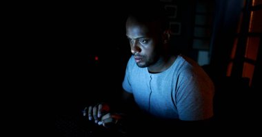 Karanlıkta dizüstü bilgisayara bakan Afrikalı bir adam. Geç saatlere kadar bilgisayar başında çalışan biri.