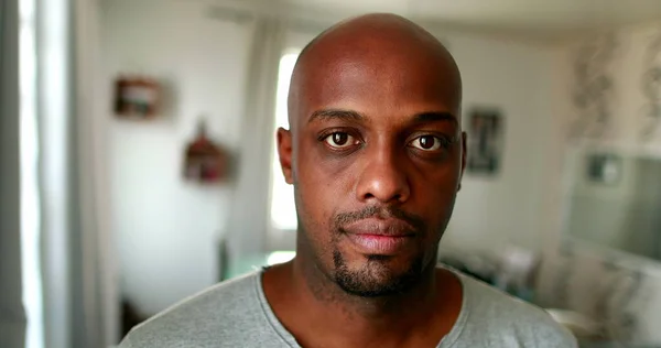 Black African man portrait looking at camera in living-room home, serious expression