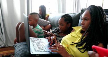 African family looking at laptop and cellphone devices at home sofa