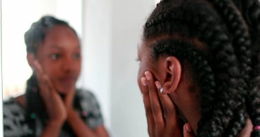 Afrikalı kız aynada kendine bakıyor. Ergenlik çağındaki kız, yansımanın karşısında duruyor.