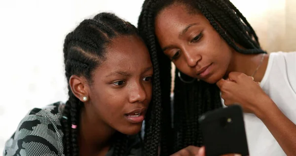 Adolescent girlfriends gossiping in front of cellphone device. Friend pointing with finger at smartphone screen