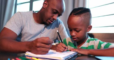 Küçük çocuk evde çalışıyor. Babasıyla birlikte ödev yapıyor.