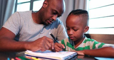 Küçük çocuk evde çalışıyor. Babasıyla birlikte ödev yapıyor.