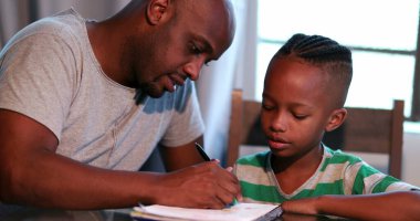 Evde ödev yapan küçük bir çocuk, Afrikalı bir baba oğlana çalışmasında yardım ediyor.