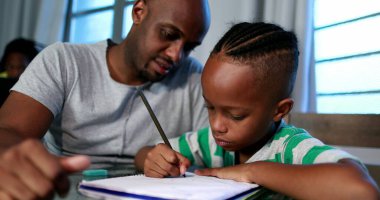 Father helping son with homework at home. African black dad mentoring little boy