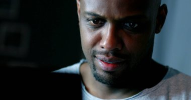 Close-up black man face looking at computer screen at night