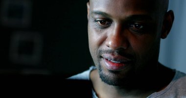 Geceleri bilgisayar ekranına bakan siyah bir adam yüzü.