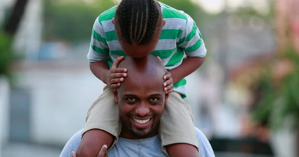 African father and son bonding. Kid kissing dad bald head, child on top of father shoulders