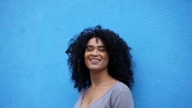 Mavi arka planda duran siyah bir kadın gülüyor ve gülümsüyor.