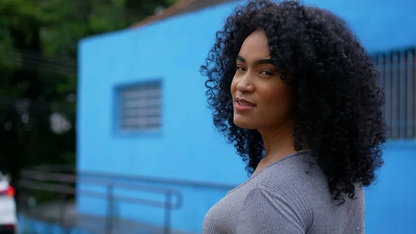 An African latina black woman walking outside in urban street turning head to camera