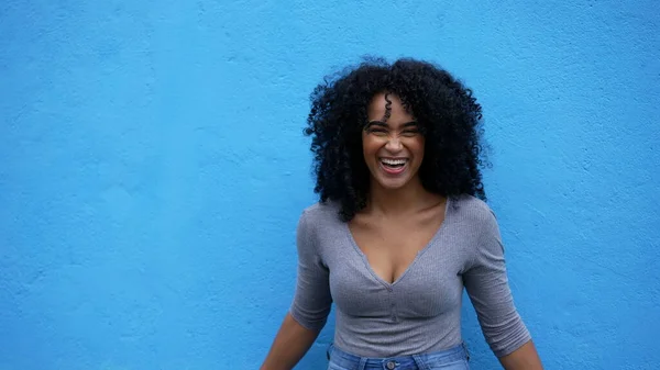 A fun loving young woman leaning on blue wall laughing and smiling