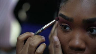 Genç siyah bir kız aynanın önünde makyaj yapıyor.