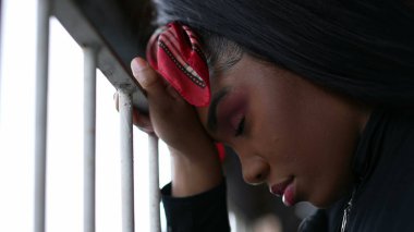 Metal çubuğa yaslanan Afrikalı bir kız gözleri kapalı pişmanlık duyuyor.