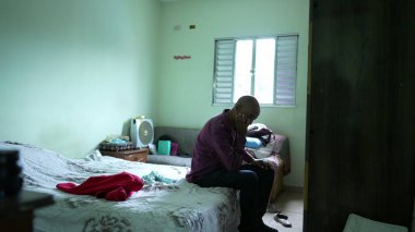 Endişeli siyah bir son sınıf öğrencisi depresyon yüzünden yatağın kenarında oturuyor.