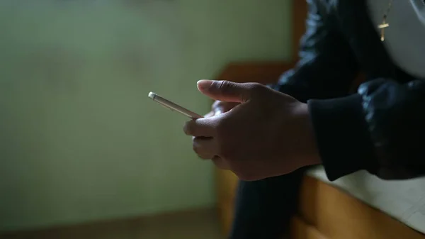 A young black man staring at phone screen sitting in bedroom using smartphone