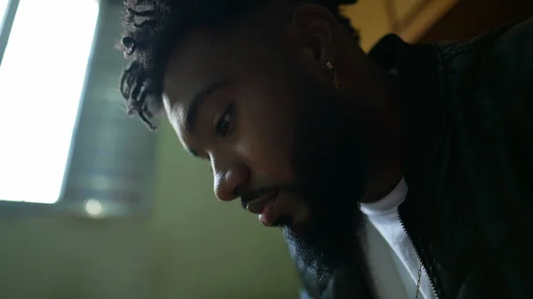 A young black man staring at phone screen sitting in bedroom using smartphone