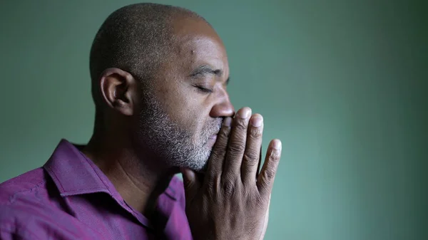 A worried senior black man praying to God seeking help. A worried senior person rubbing face with hands feeling hopeless