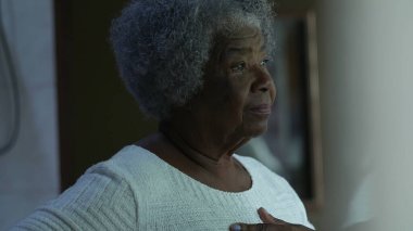 Endişeli yaşlı siyahi bir kadın pencerenin kenarında durmuş endişeli bir Afrikalı yaşlı bayana bakıyor.