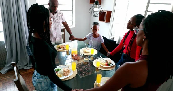 Religious African family gathered together in prayer before eating