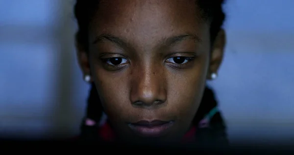 Teenager looking at computer screen at night browsing internet, black African ethnicity teen girl studying