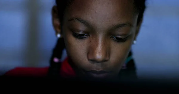 Teenager looking at computer screen at night browsing internet, black African ethnicity teen girl studying