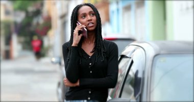 Siyah bir genç cep telefonuyla dışarıda arama yapıyor.