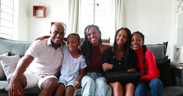 Beautiful Black African family sitting at couch smiling at camera, parents and children
