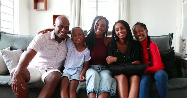 Beautiful Black African family sitting at couch smiling at camera, parents and children