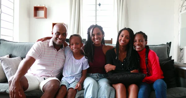 Beautiful Black African family sitting at couch smiling at camera, parents and children