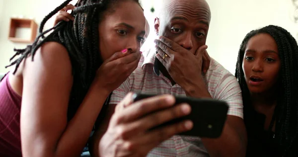 African family shock reaction looking at cellphone device. parents and children surprise reaction to smartphone news