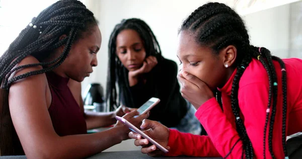 Concerned teen black girl looking at cellphone social media. African family staring at screens each in their own bubble