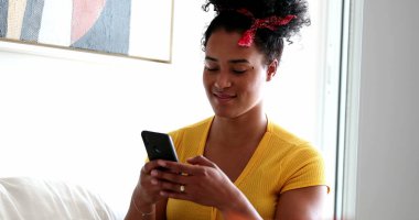 Gülümseyen cep telefonu aygıtı kullanan gizli bir zenci kız. Genç bir kadın evde oturuyor ve telefonda yazıyor.