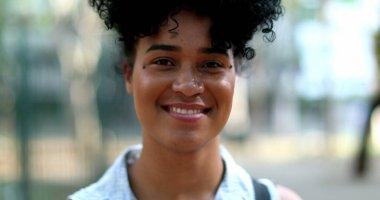 Karışık ırktan genç bir kadın dışarıda gülümsüyor.