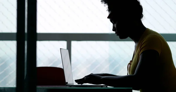 Silhouette young black woman typing on laptop computer at home