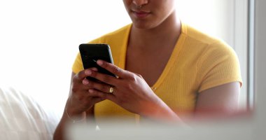 Genç siyahi bir kadın akıllı telefon cihazıyla yazı yazıyor. Samimi bir kız evde cep telefonu kullanıyor.