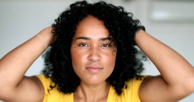 Genç siyahi kadın kameraya bakıyor. Saçlarını düzeltiyor. Afrikalı Amerikalı kız dışarı çıkmaya hazırlanıyor.