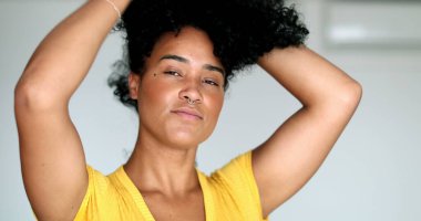 Genç siyahi kadın kameraya bakıyor. Saçlarını düzeltiyor. Afrikalı Amerikalı kız dışarı çıkmaya hazırlanıyor.