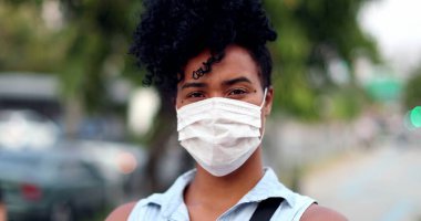 Karışık ırktan bir kadın şehir arka planında covid-19 yüz maskesi takıyor.