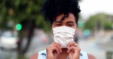 Karışık ırktan bir kadın şehir arka planında covid-19 yüz maskesi takıyor.