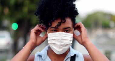 Karışık ırktan bir kadın şehir arka planında covid-19 yüz maskesi takıyor.