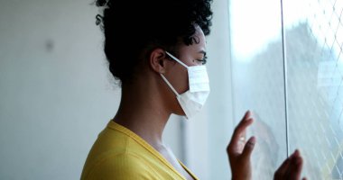 Pencere kenarında duran Afrikalı kadın virüse karşı salgın maskesi takıyor.